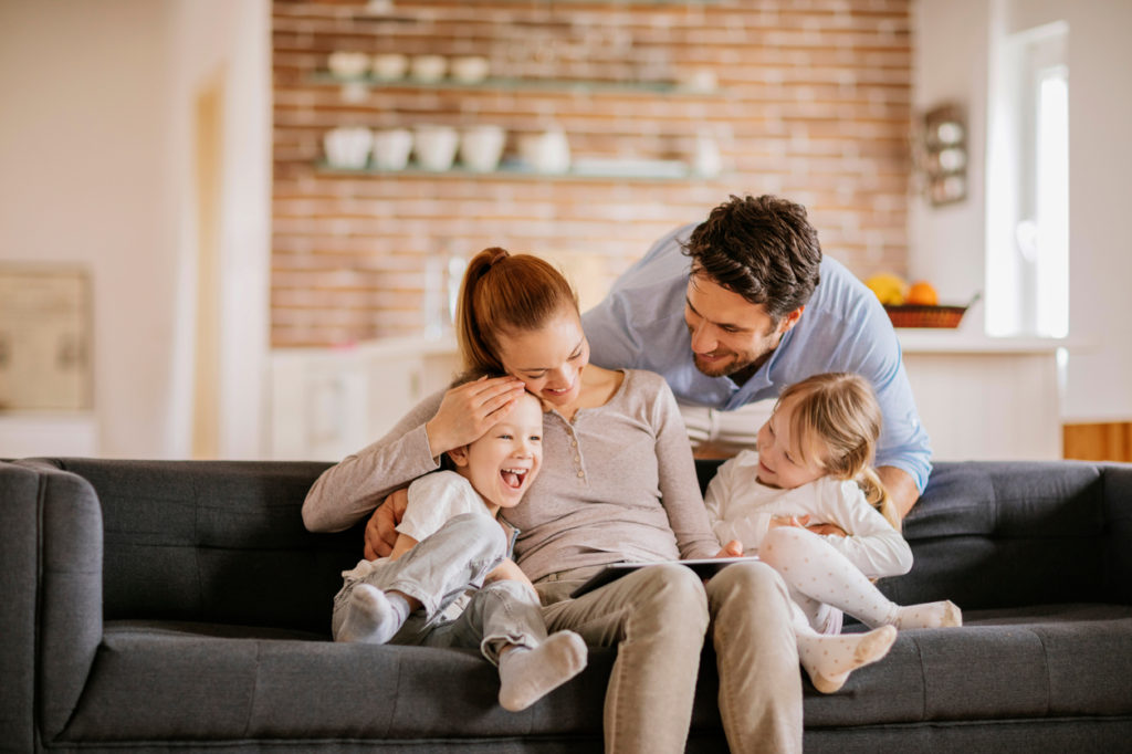 Happy young family sitting in living room – Chesapeake Comfort Systems